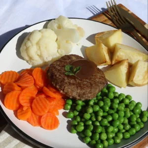 Rissole with gravy, roast potatoes, carrots, peas, and cauliflower