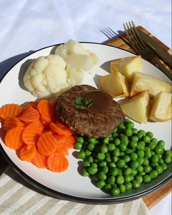 Rissole with gravy, roast potatoes, carrots, peas, and cauliflower