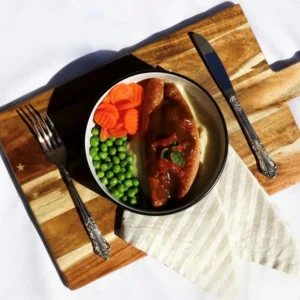 Sausages on mash potato with tomato and onion gravy, carrots and peas