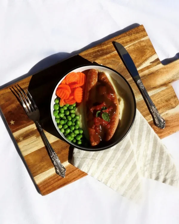 Sausages on mash potato with tomato and onion gravy, carrots and peas